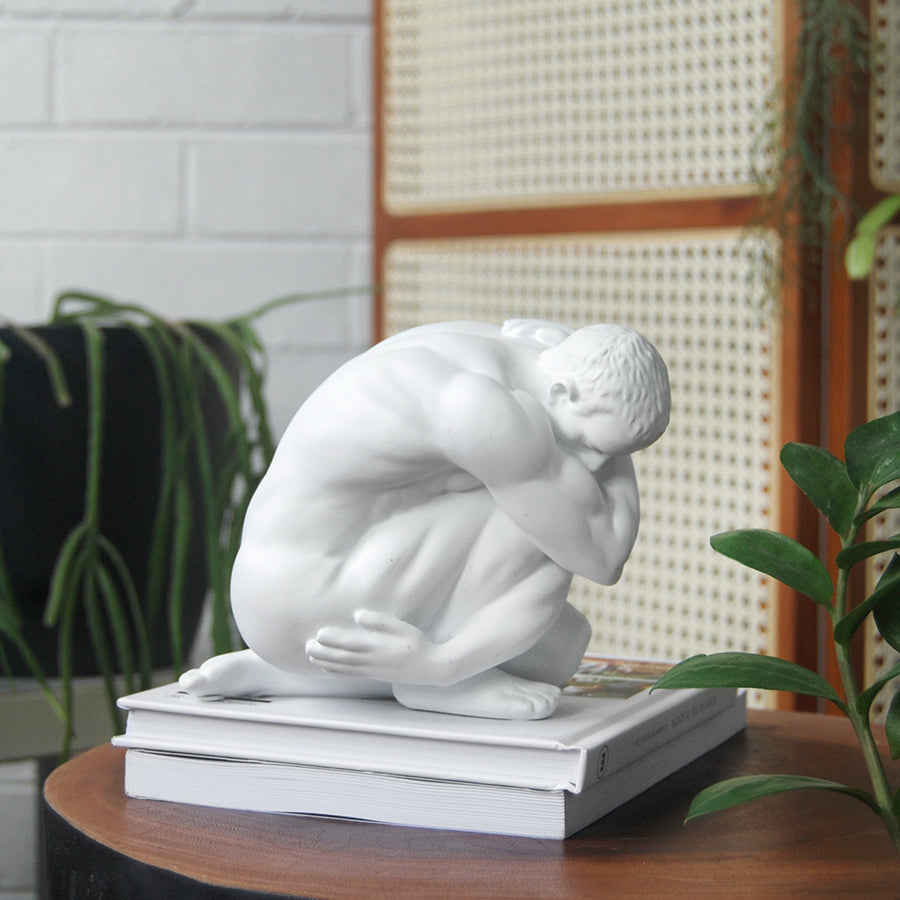 White resin sculpture of crouching male figure styled on a stack of books