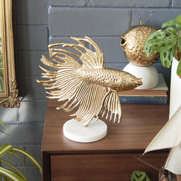 Gold betta fish sculpture on white base displayed on wooden console