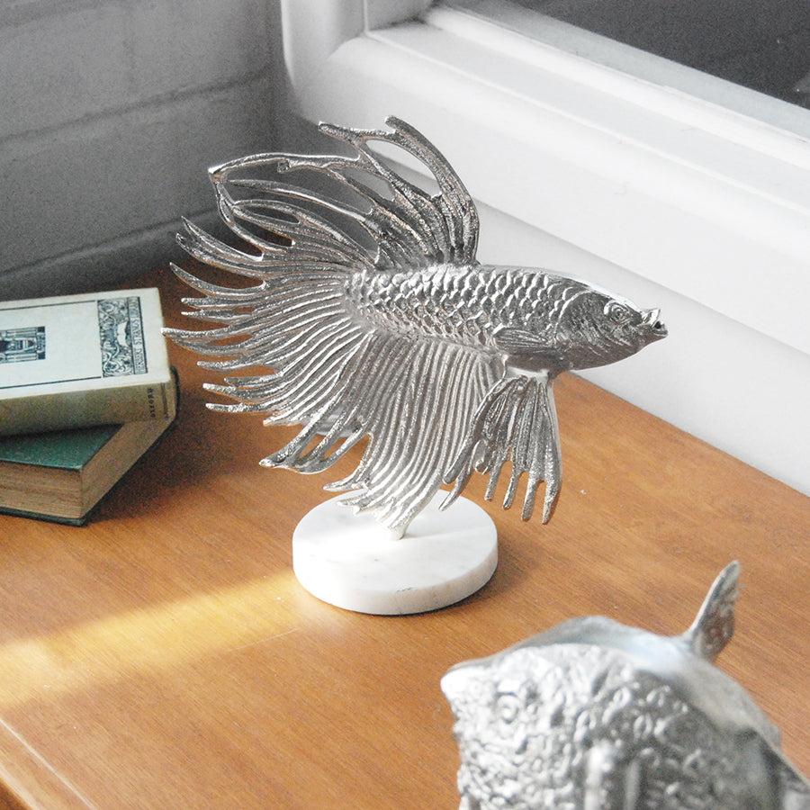 Sculptural silver betta fish décor piece on marble-look base indoors