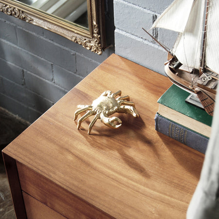 Gold crab sculpture styled on a wooden console next to books and nautical décor