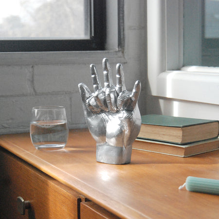 Decorative silver hands sculpture styled near books