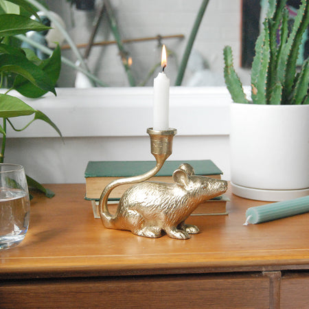 Gold mouse-shaped candle holder with lit taper candle on wooden console