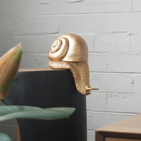 Gold resin snail sculpture perched on the edge of a black and timber console