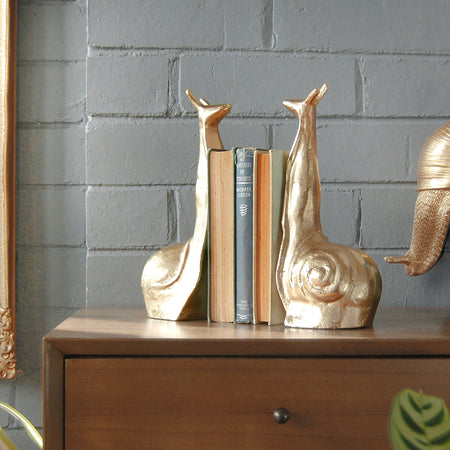 Gold snail bookends displayed with upright books on timber furniture