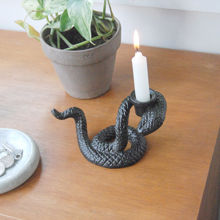 Black snake-shaped candle holder with lit taper candle on wooden surface