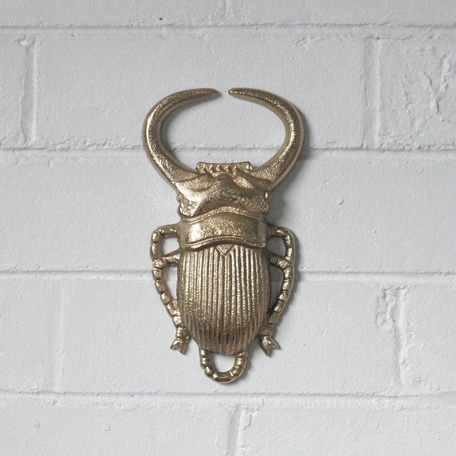 Metallic gold beetle wall décor on white brick wall