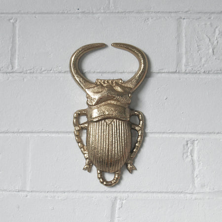 Metallic gold beetle wall décor on white brick wall