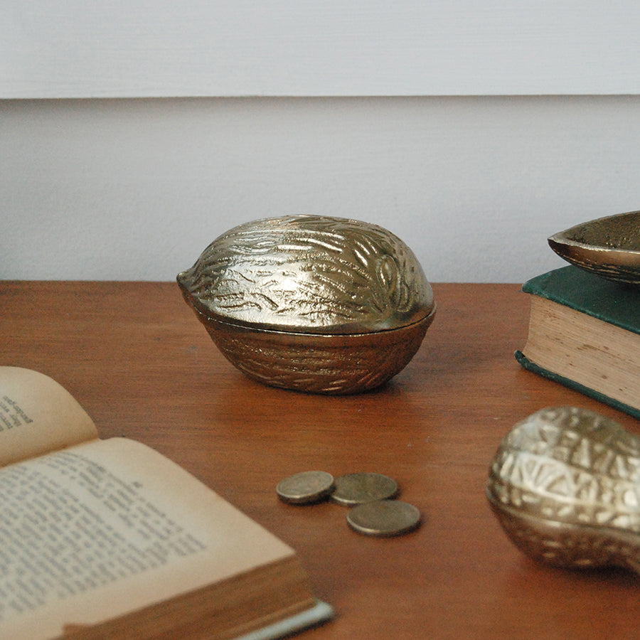 Gold walnut-shaped trinket box displayed on wooden surface with books