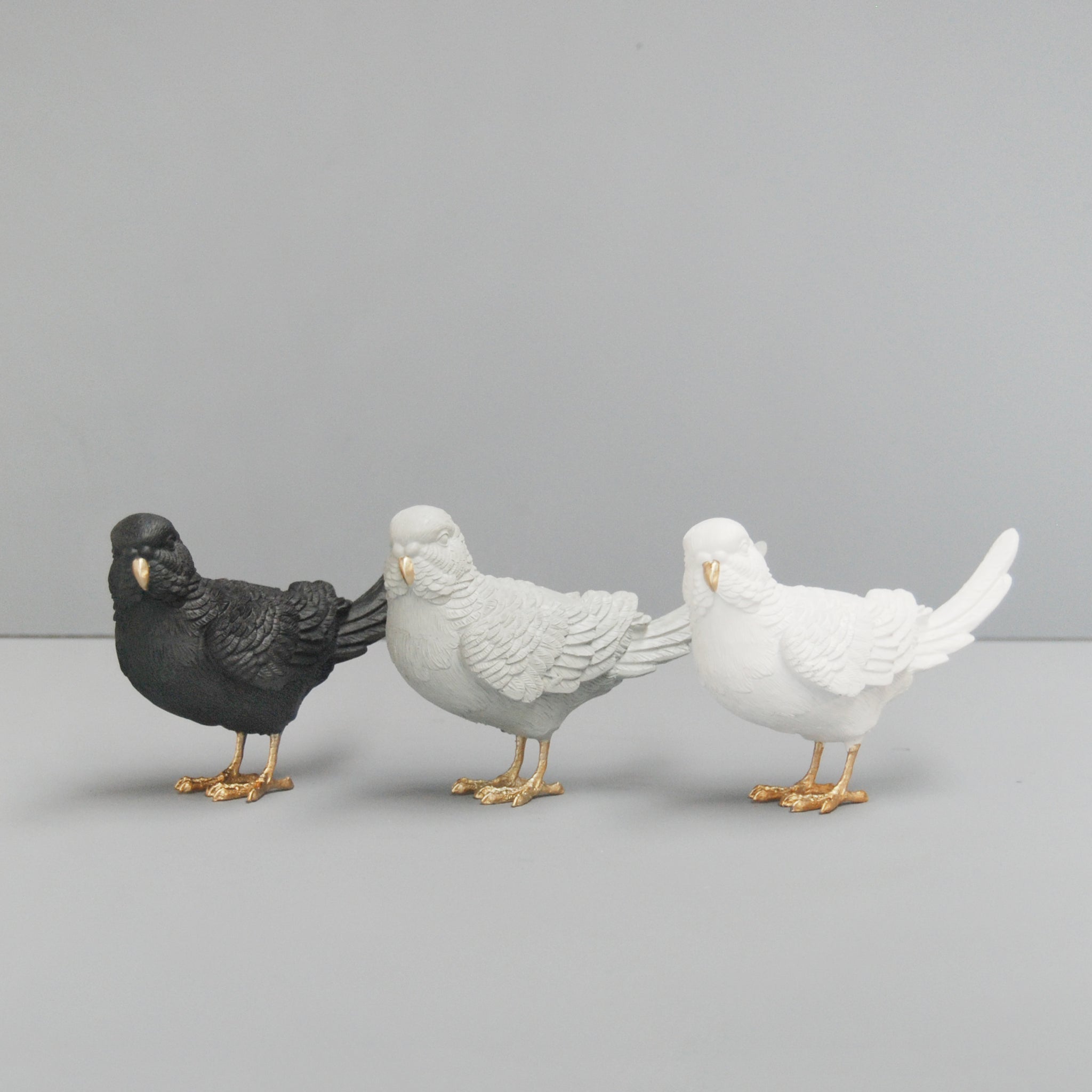Set of three resin budgie sculptures in black, grey, and white with gold accents
