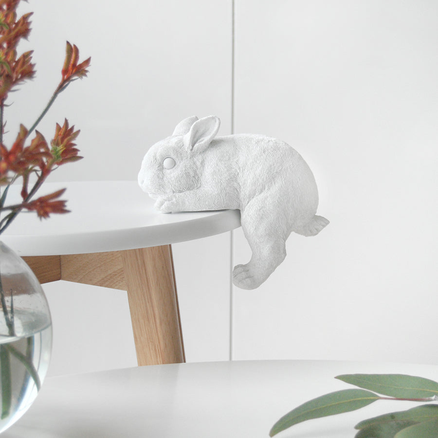 White resin bunny sculpture hanging gently off the edge of a round table
